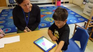 Josey Redinger, NC Pre-K teacher at Central Davie Preschool watches as preschool student Alan Reyes works with Cognitive ToyBox