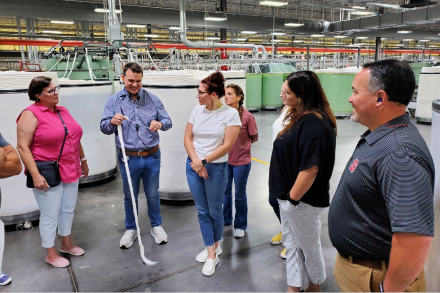 (L to R) Melanie White, Chelsea Dvorak, Hannah Beck, Amy Hardister, Dianne Ireland, and Anthony Davis look on as John Lane, assistant plant manager, explains how Gildan turns cotton into yarn. 