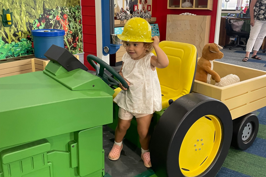 The COGNITION ribbon-cutting’s youngest attendee, Cooper Brown sits on a green tractor in the COGNITION Play area